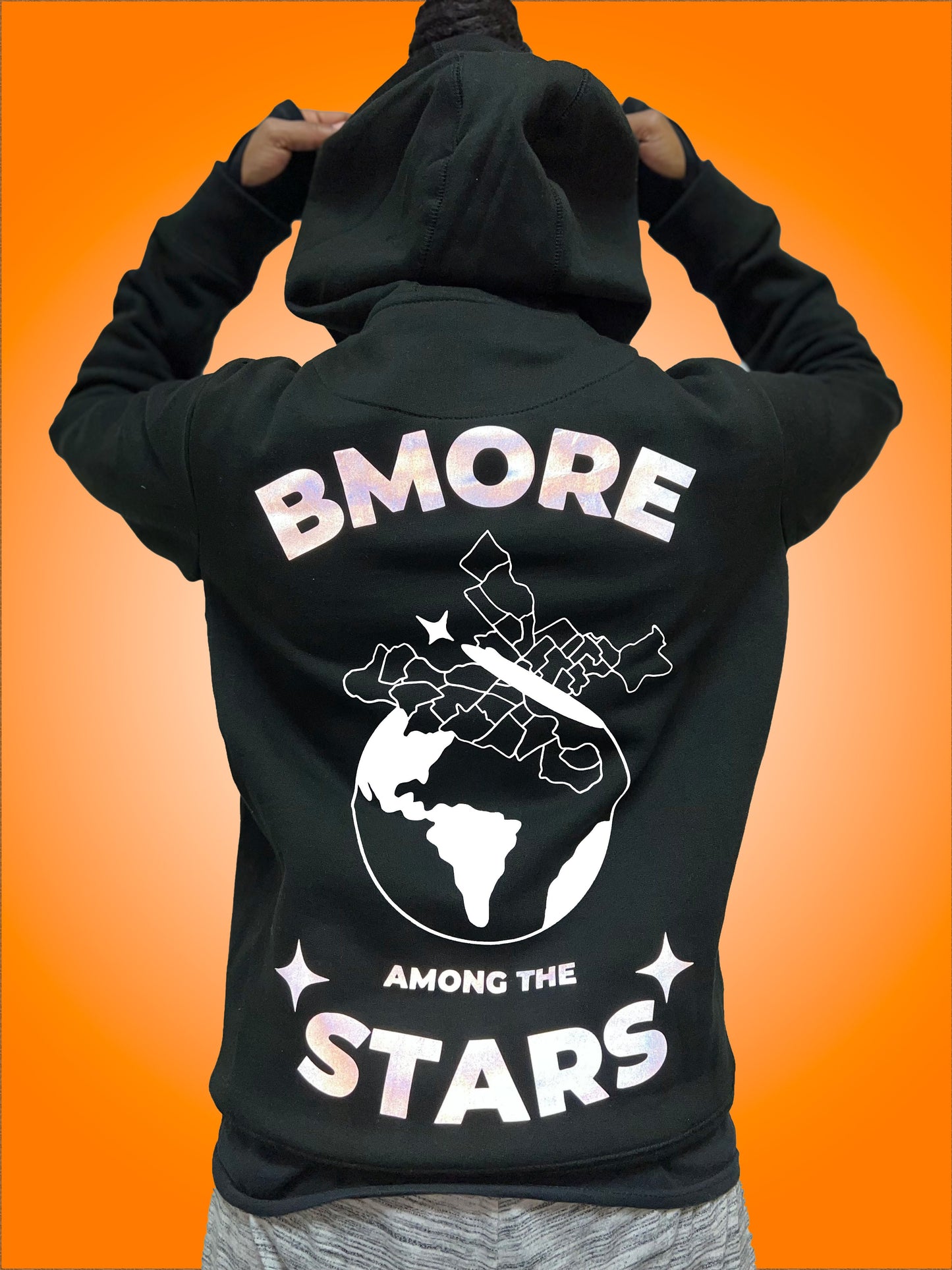 Back of  black hoodie. In reflective, gray, shimmering  vinyl: "BMore" written in curved down, bold letters at top, "Among the", written along the bottom over Stars which is slightly curved up, bold letters the same size as "Bmore". 2  stars on the outside of the word "Stars". The lettering and stars are all in reflective gray vinyl that shimmered. In between is the "Black Butterfly", a design which has West & East Baltimore neighborhoods outlined, sitting on top of the world 